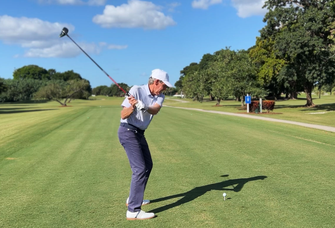 Golfer, mid swing, teeing off from a sunny tee box into a well groomed fairway.